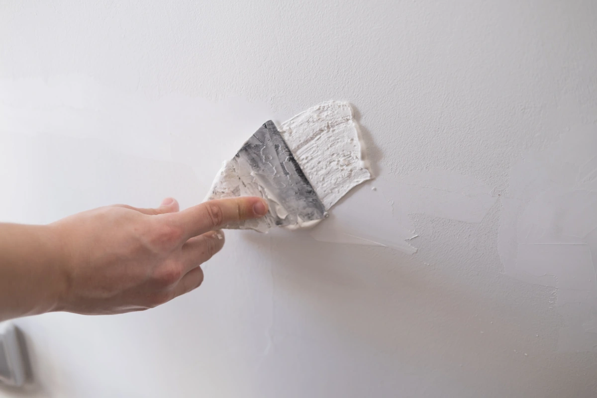Une personne qui applique unepâte d'enduit de rebouchage sur un mur en placo